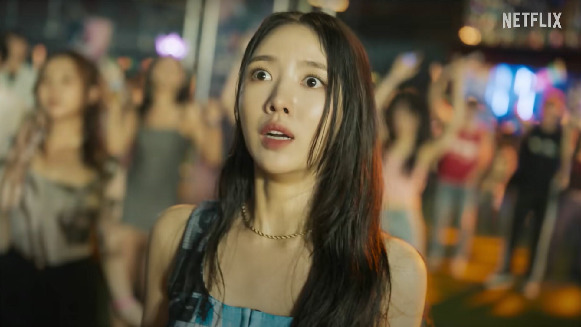 A woman standing in a crowd looks shocked and scared.